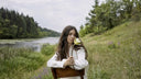 Woman in white cotton outfit sitting in a field with a water lily, eyes closed — MOSAÏKA