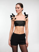 Black strapless crop top by MOSAÏKA styled with detachable feather straps creating sculptural shoulder detail